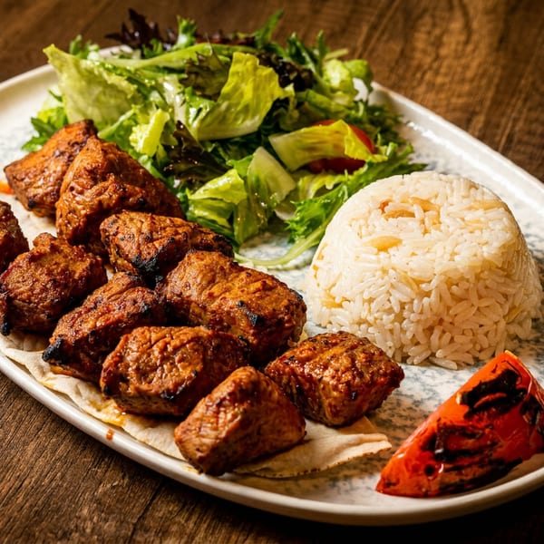 Grilled meat skewers with rice, fresh salad, and a roasted tomato on a white plate.