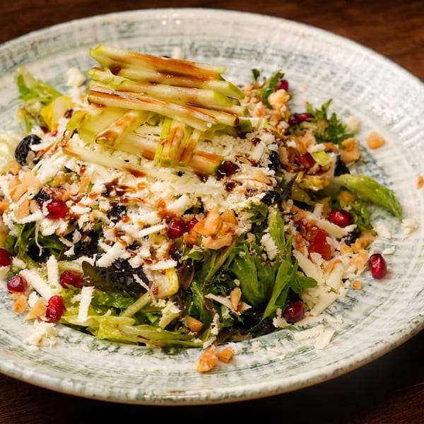 Fresh green salad with shredded cheese, pomegranate seeds, nuts, and apple slices on a plate.